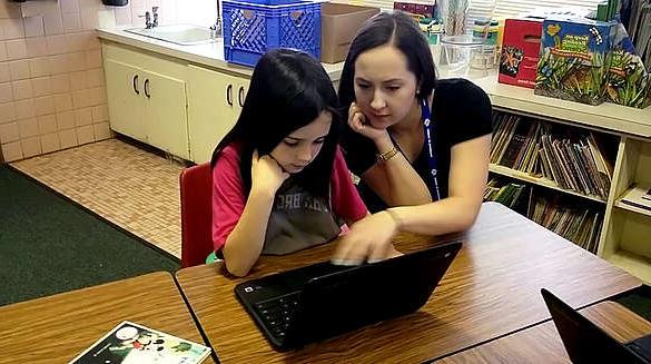 student teacher working with young student on laptop